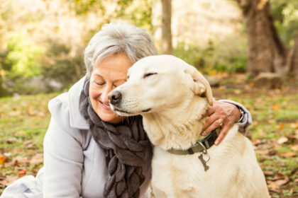 Une femme senior colle son visage contre la tête de son chien qui plisse les yeux de bonheur. Sa présence apporte beaucoup dans le quotidien pour un senior