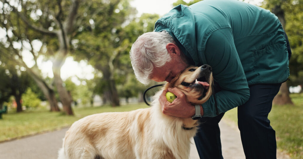 Un homme embrasse son chien golden retriever sur la tête en l'enlaçant et en tenant une balle de tennis dans la main.