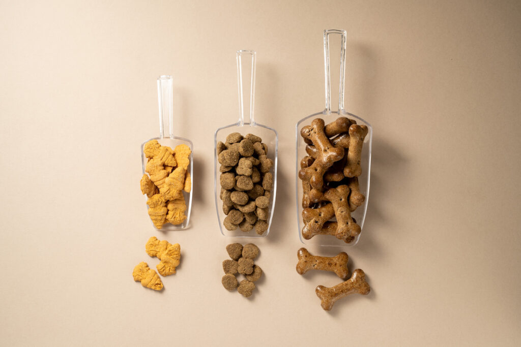 Trois pelles avec chacune différents type de croquettes ou de friandises pour chien. L'alimentation représente une part importante du budget pour un animal de compagnie.